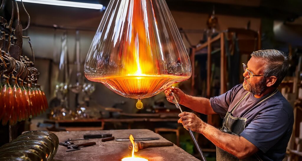 Glassmaker using traditional tools to shape molten glass into a hand blown chandelier, showcasing the artistry and craftsmanship behind the creation process