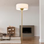 A sleek and elegant modern floor lamp, inspired by mid-century design, featuring a glossy brass finish, a tall slender frame, and a round silk shade in soft white, set against a minimalistic interior backdrop with neutral tones and contemporary furniture.